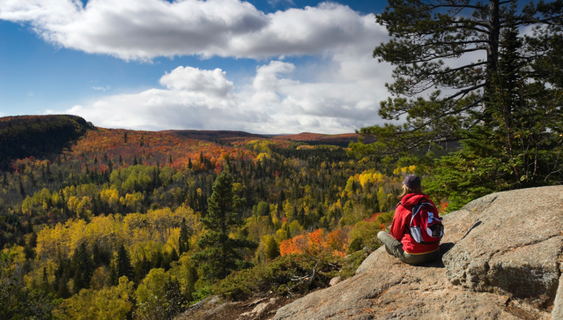 Female hiker sitting on rocky ledge taking in a scenic Autumn view in Minnesotas Arrowhead region from Oberg Mountain.