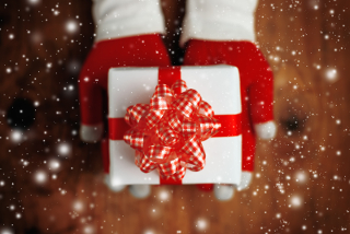 Woman offering Christmas gift in wrapped box holiday season with snowflakes falling top view retro toned image with selective focus